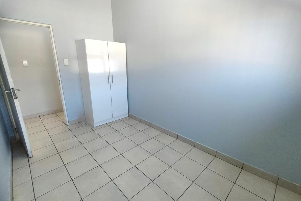 A simple, empty bedroom featuring neutral wall paint and light-colored floor tiles, providing a clean and versatile space ready for personalization.