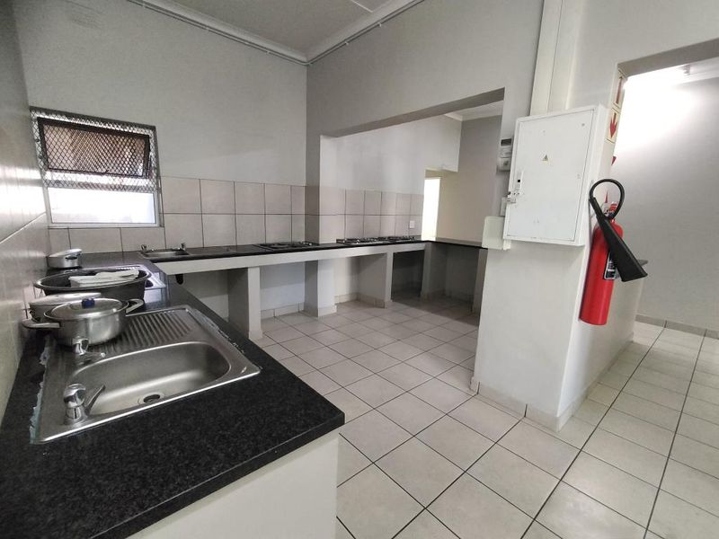A functional kitchen area featuring tiled flooring, a built-in sink, and extensive countertop space, currently awaiting cabinetry installation or renovation.