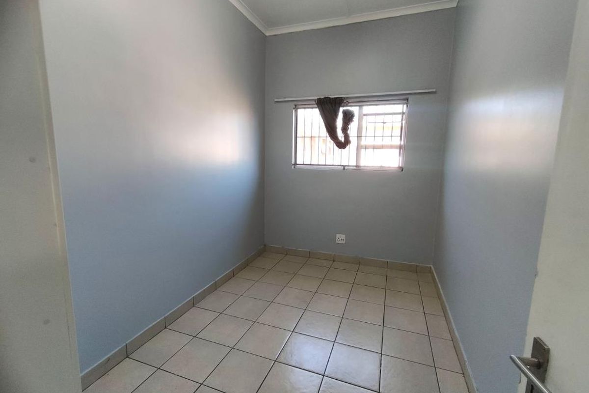 A clean, empty bedroom featuring neutral grey walls, tiled flooring, and a window fitted with security bars.