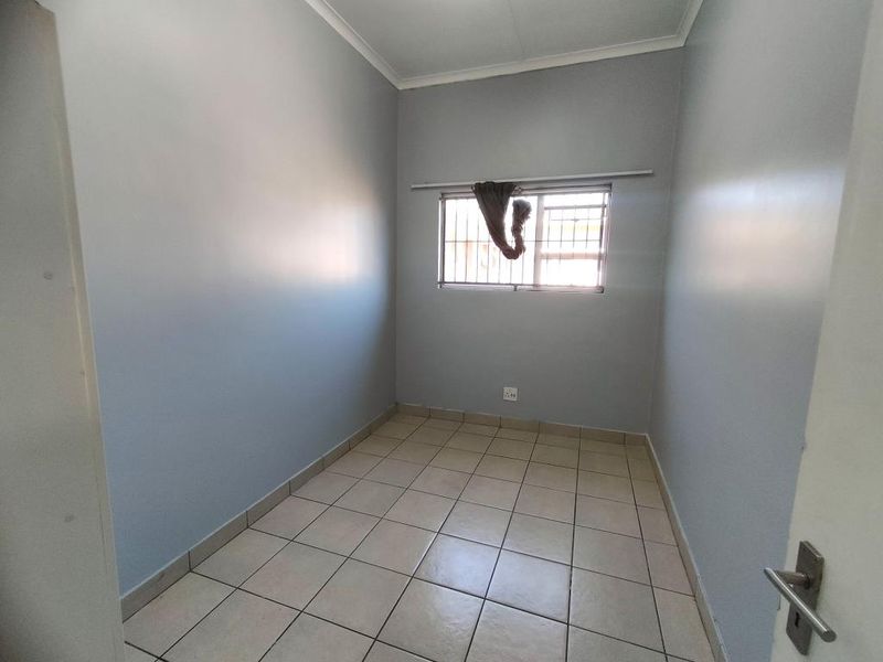 A clean, empty bedroom featuring neutral grey walls, tiled flooring, and a window fitted with security bars.