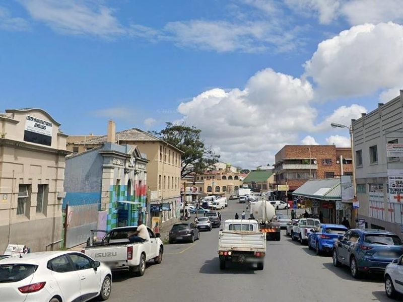 A street-level view of a busy urban commercial area featuring various storefronts and mixed-use buildings along the road.