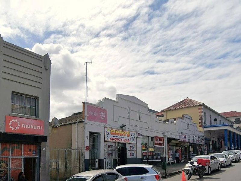 A street-level view of a commercial building row featuring multiple storefronts with signage and security fixtures along a busy urban road.