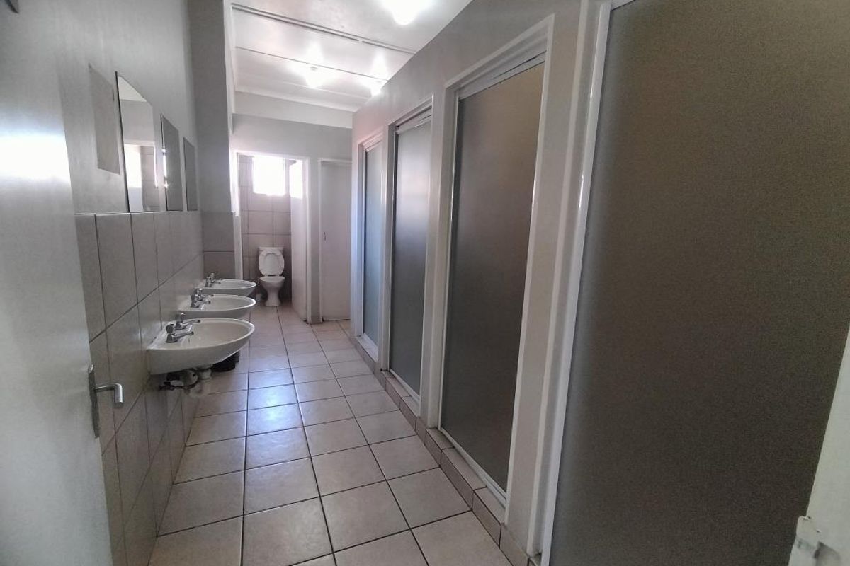 A communal-style bathroom facility featuring multiple wall-mounted washbasins, tiled flooring, and private stalls with frosted glass doors.