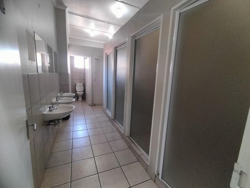 A communal-style bathroom facility featuring multiple wall-mounted washbasins, tiled flooring, and private stalls with frosted glass doors.