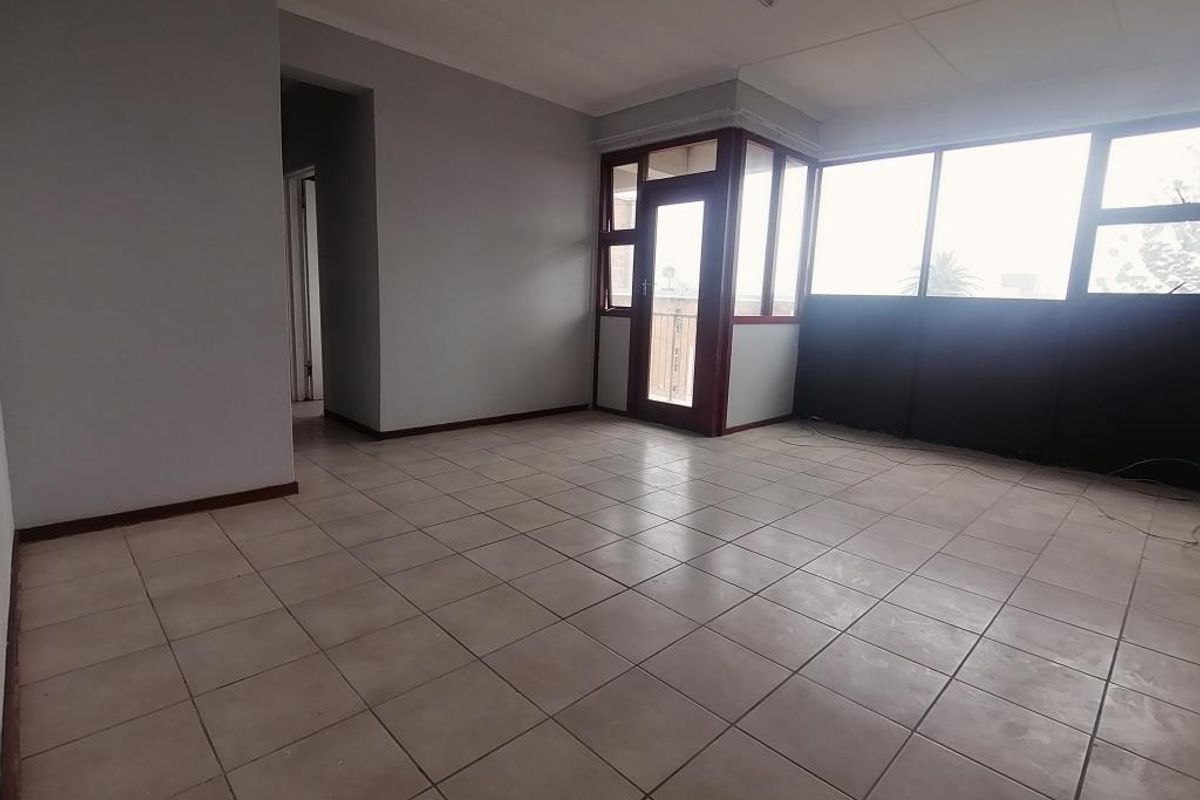 An empty, open-plan living area featuring neutral tiled flooring, large windows, and a glass-panelled door leading to an outdoor space.