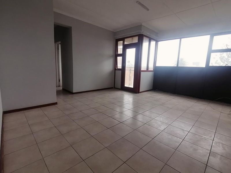 An empty, open-plan living area featuring neutral tiled flooring, large windows, and a glass-panelled door leading to an outdoor space.