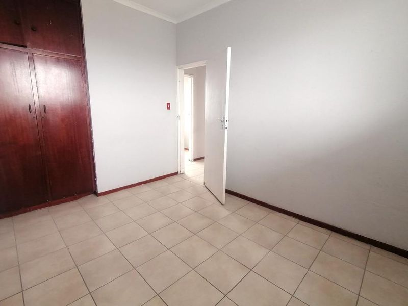 An empty bedroom featuring tiled flooring and built-in wooden cupboards, offering a blank canvas for personalization.