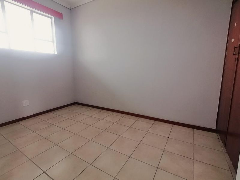 A vacant bedroom featuring neutral tiled flooring, a built-in cupboard, and a window providing natural light.