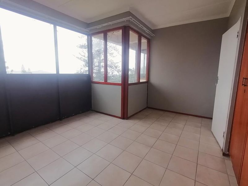An enclosed balcony featuring tiled flooring, large windows with aluminium frames, and a built-in cupboard, offering a versatile space with natural light.