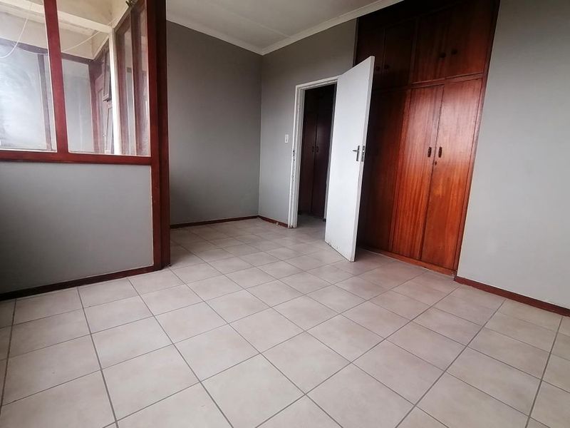 An empty bedroom featuring tiled flooring, built-in wooden cupboards, and an internal glass partition wall.