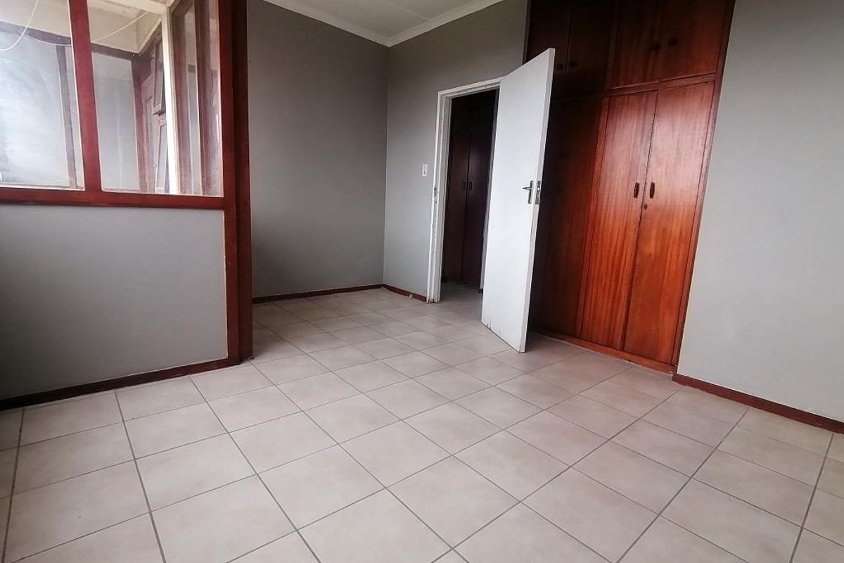 An empty bedroom featuring tiled flooring, built-in wooden cupboards, and an internal glass partition wall.