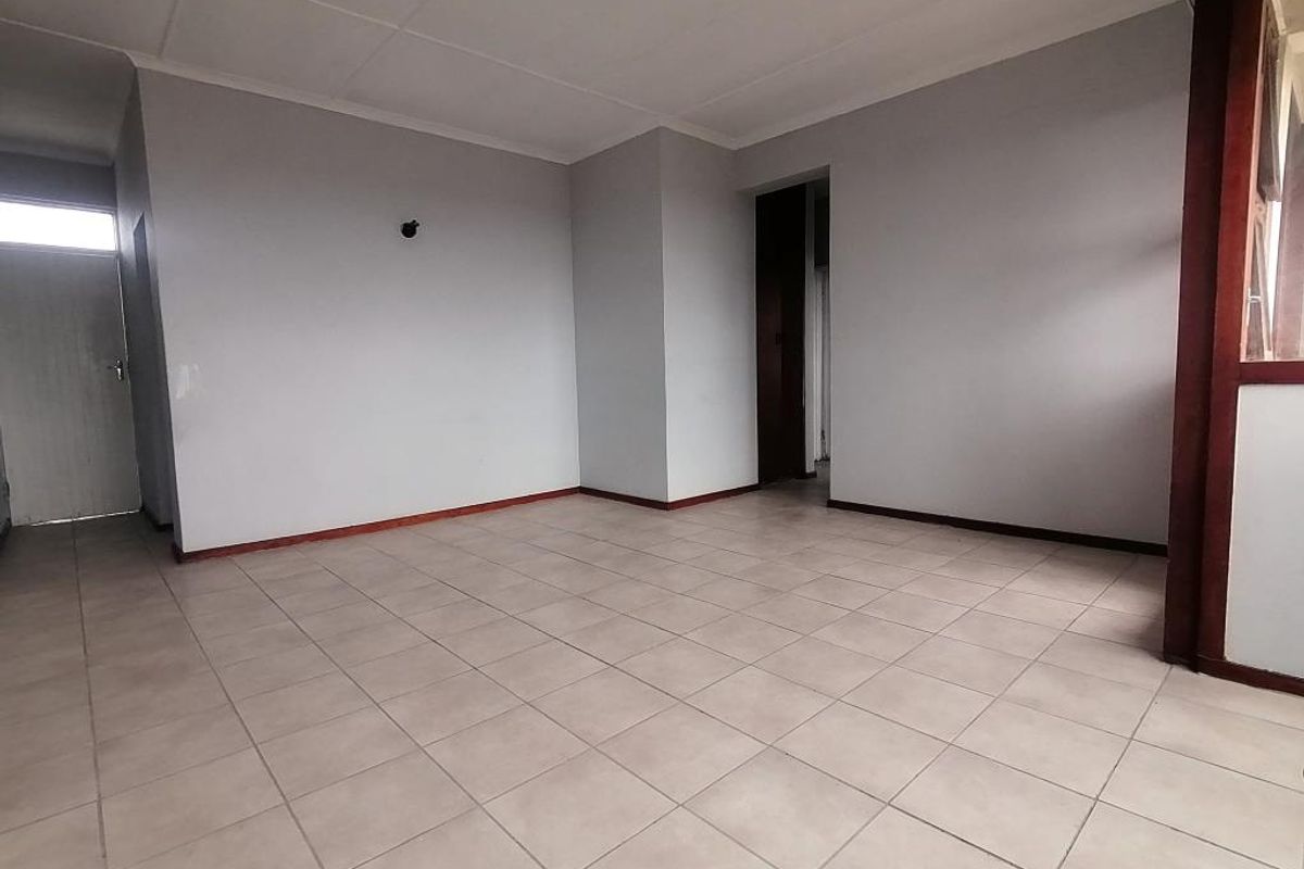 An empty, open-plan living area featuring neutral ceramic floor tiles, coved ceilings, and simple wall finishes, ready for personalization.