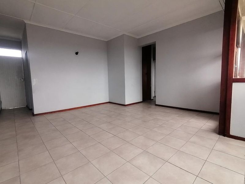 An empty, open-plan living area featuring neutral ceramic floor tiles, coved ceilings, and simple wall finishes, ready for personalization.