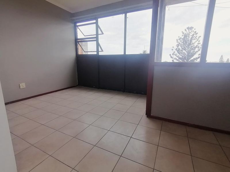 An empty, enclosed balcony featuring tiled flooring and large aluminium-framed windows, offering a versatile space with potential for a sunroom or study area.