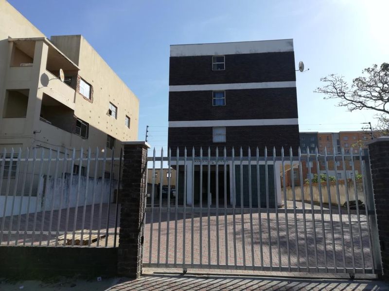Front view of a multi-story apartment building featuring a secure metal gate and paved driveway access.