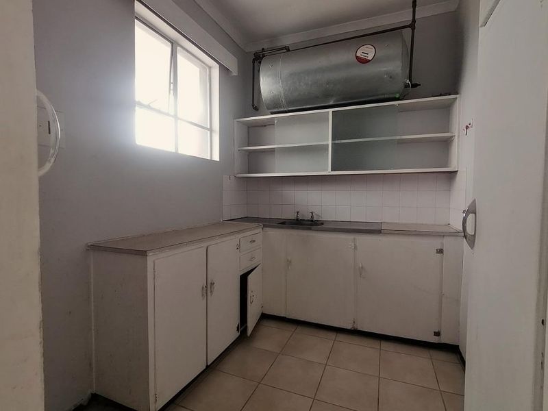 A functional laundry room featuring built-in cabinetry, a stainless steel sink, tiled splashback, and an overhead electric water heater.