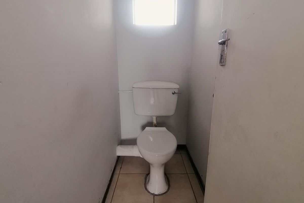 A compact, functional bathroom featuring a standard toilet, tiled flooring, and a small window for natural light.