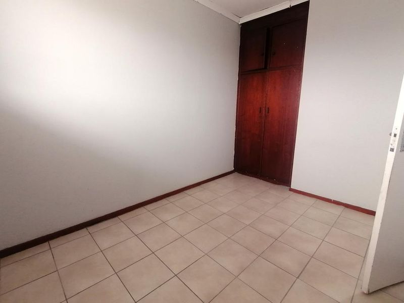 An empty bedroom featuring tiled flooring and a built-in wooden cupboard, offering a blank canvas for potential renovation or staging.