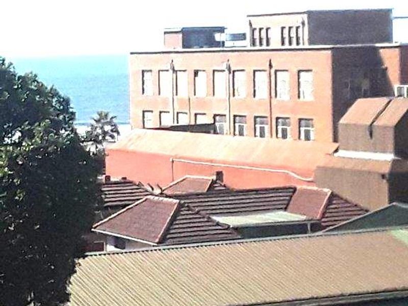 An elevated view overlooking surrounding urban rooftops and buildings with a glimpse of the ocean in the distance.