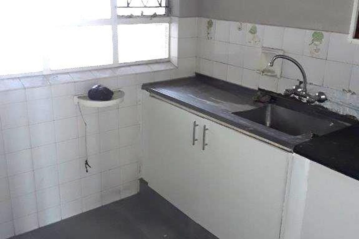 A compact, empty kitchen featuring a stainless steel sink, laminate countertops, and tiled splashbacks, offering a functional space ready for modernization.
