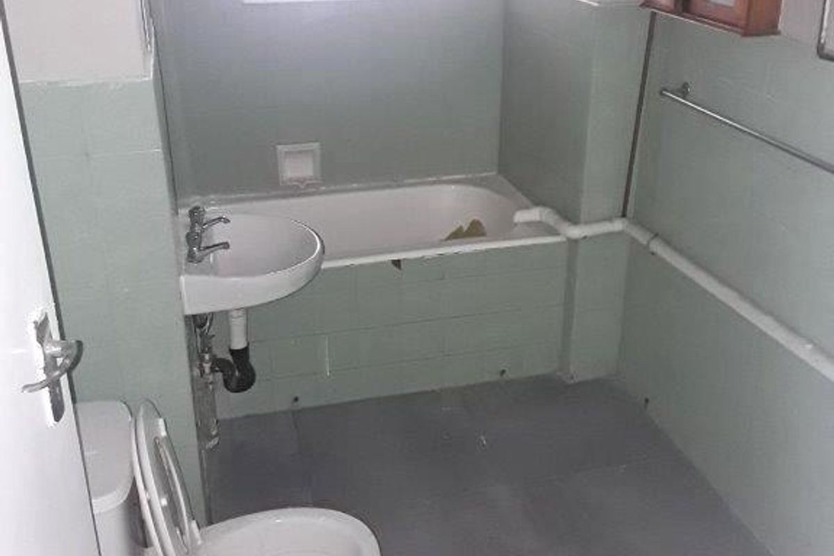 A dated bathroom featuring a bathtub, pedestal basin, and toilet with exposed plumbing and tiled finishes, offering potential for modernization.