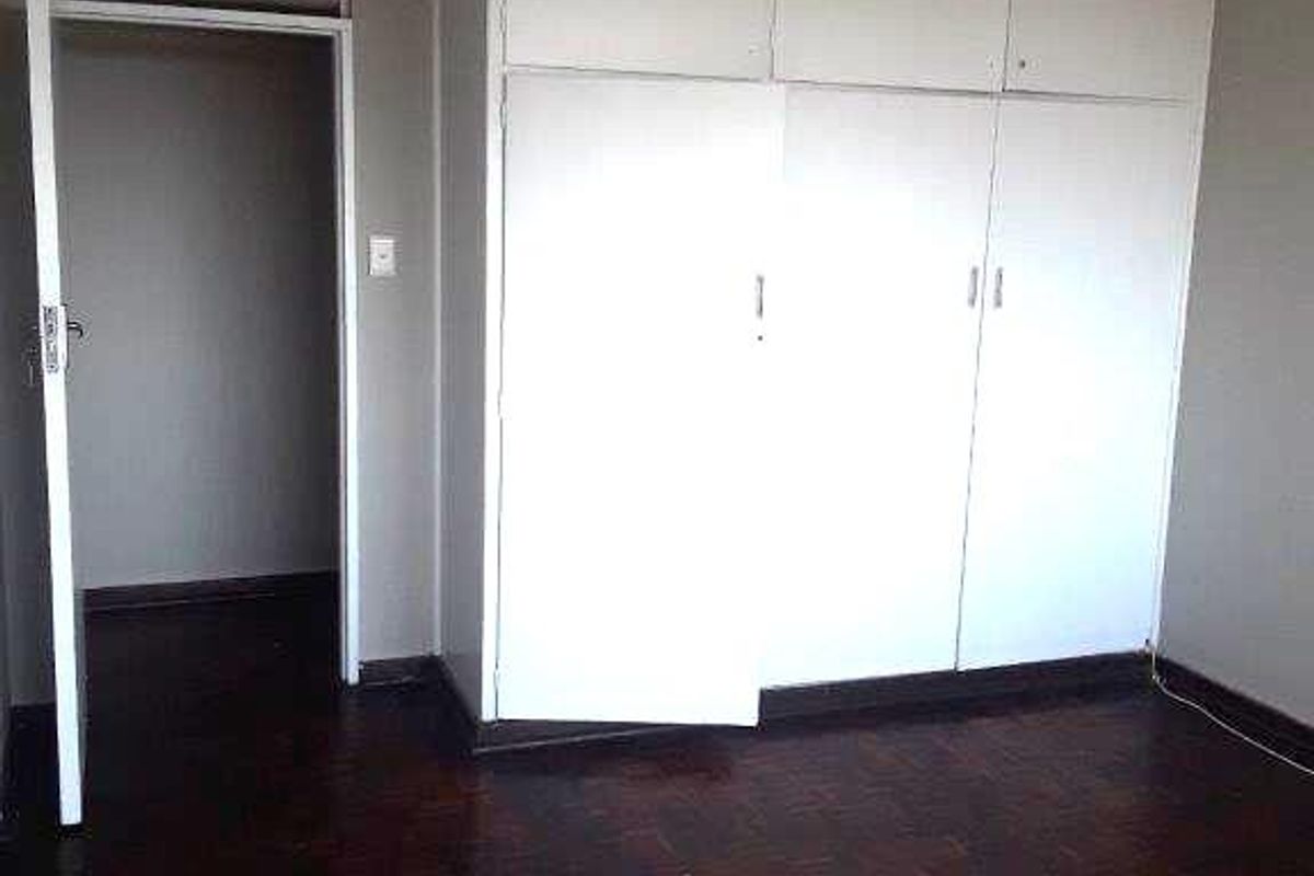 A vacant bedroom featuring dark parquet flooring and ample built-in cupboard storage space.