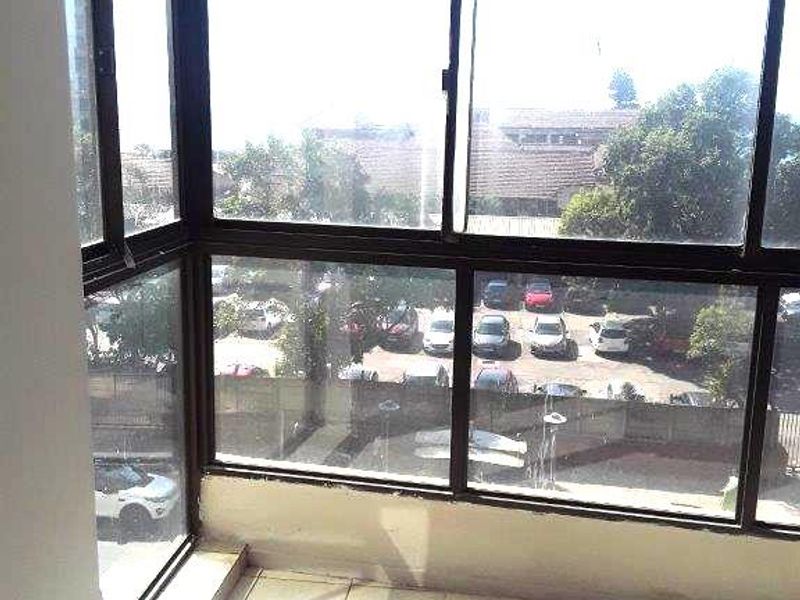 An enclosed balcony or sunroom featuring tiled flooring and large aluminium-framed windows with views over the parking area.