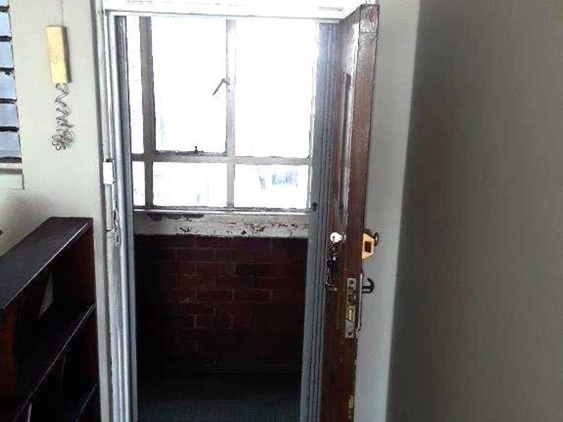 A small, enclosed balcony area featuring brick wall detailing, tiled flooring, and a metal-framed window, currently in need of cosmetic refurbishment.