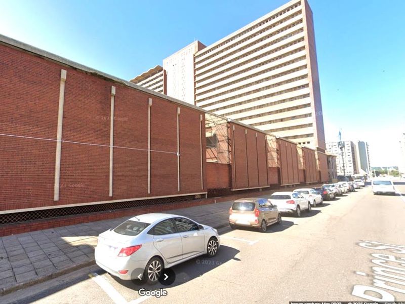 Street level view of a large brick apartment building facade with adjacent parking and sidewalk.