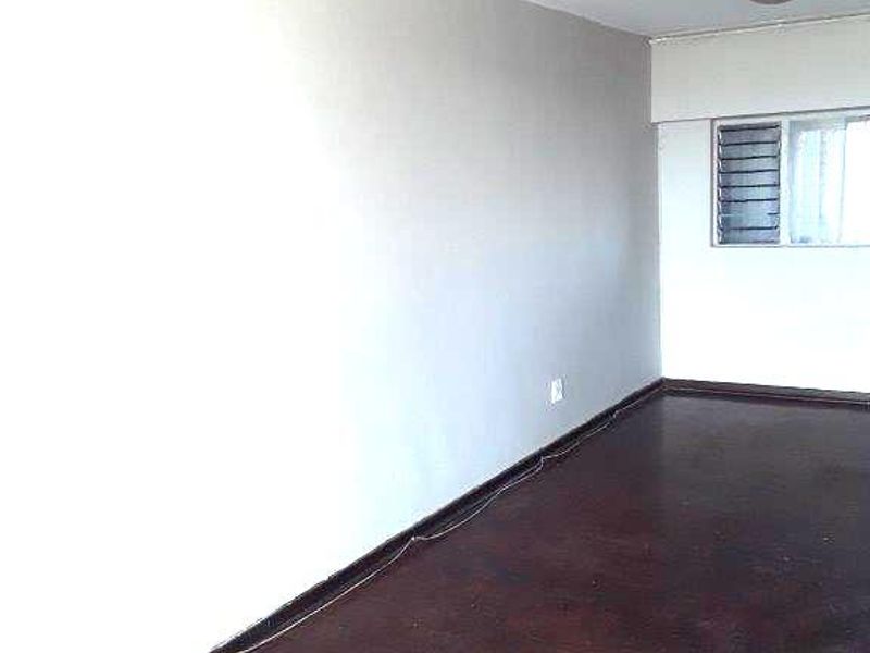 An empty living room featuring dark parquet flooring, a louvered window, and neutral wall paint, offering a blank canvas for interior design.