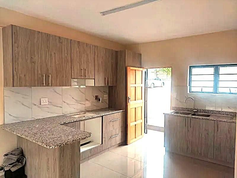 A modern, empty kitchen featuring granite countertops, light wood-grain cabinetry, tiled backsplash, and direct access to the exterior.