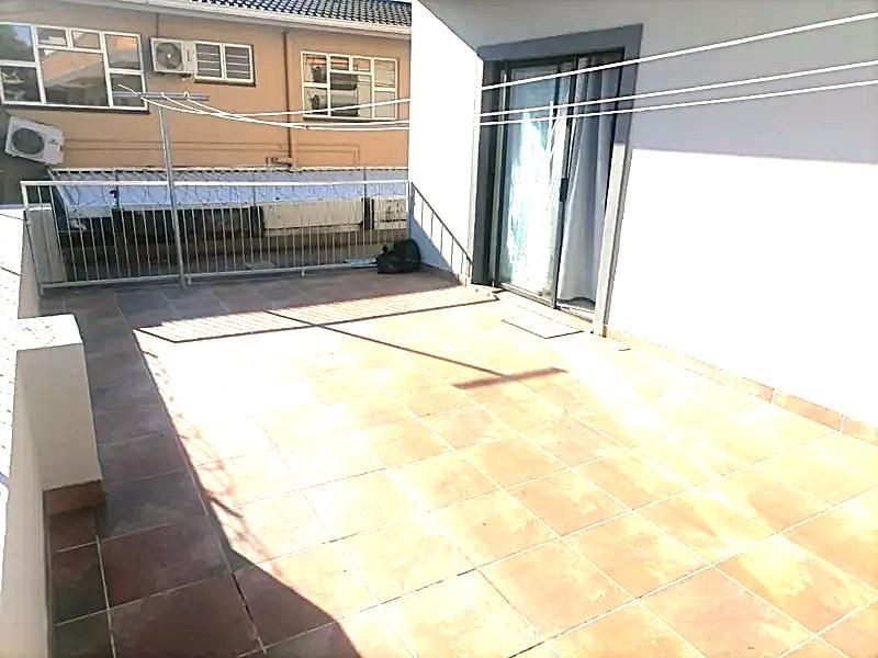 A spacious open balcony featuring tiled flooring, a metal safety balustrade, and direct access to the interior through a sliding glass door.