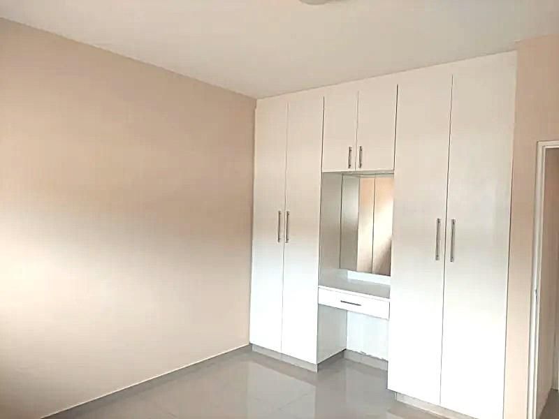 A clean, empty bedroom featuring modern white built-in cupboards with an integrated vanity station and neutral tiled flooring.