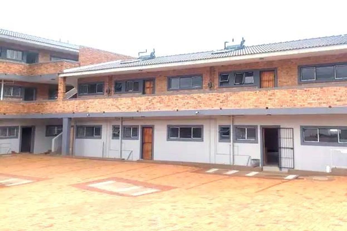 Exterior view of a multi-story apartment complex featuring face brick construction, paved courtyard, and solar geyser installations on the roof.