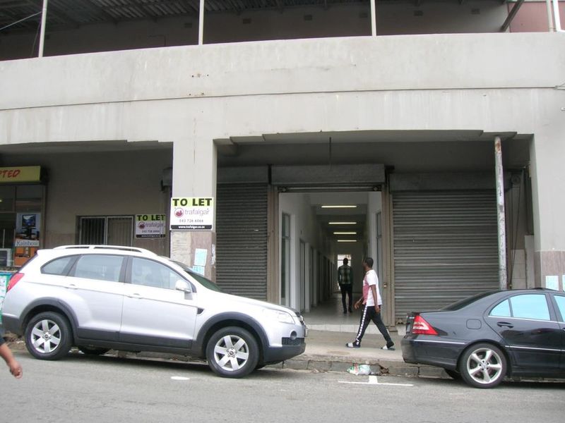 Commercial building frontage featuring roller shutter doors and a covered entrance walkway with fluorescent lighting.
