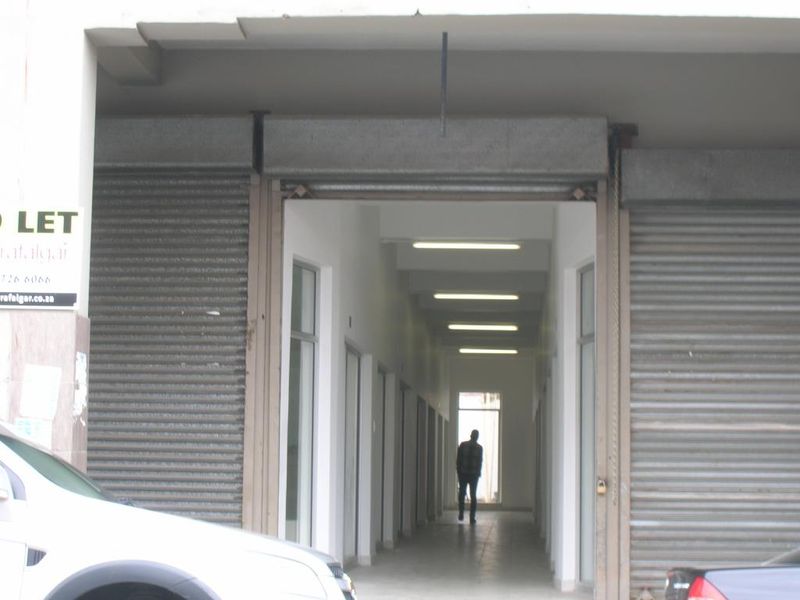 Commercial building entrance featuring roller shutter doors and a long hallway with glass-paneled doors leading to the interior.