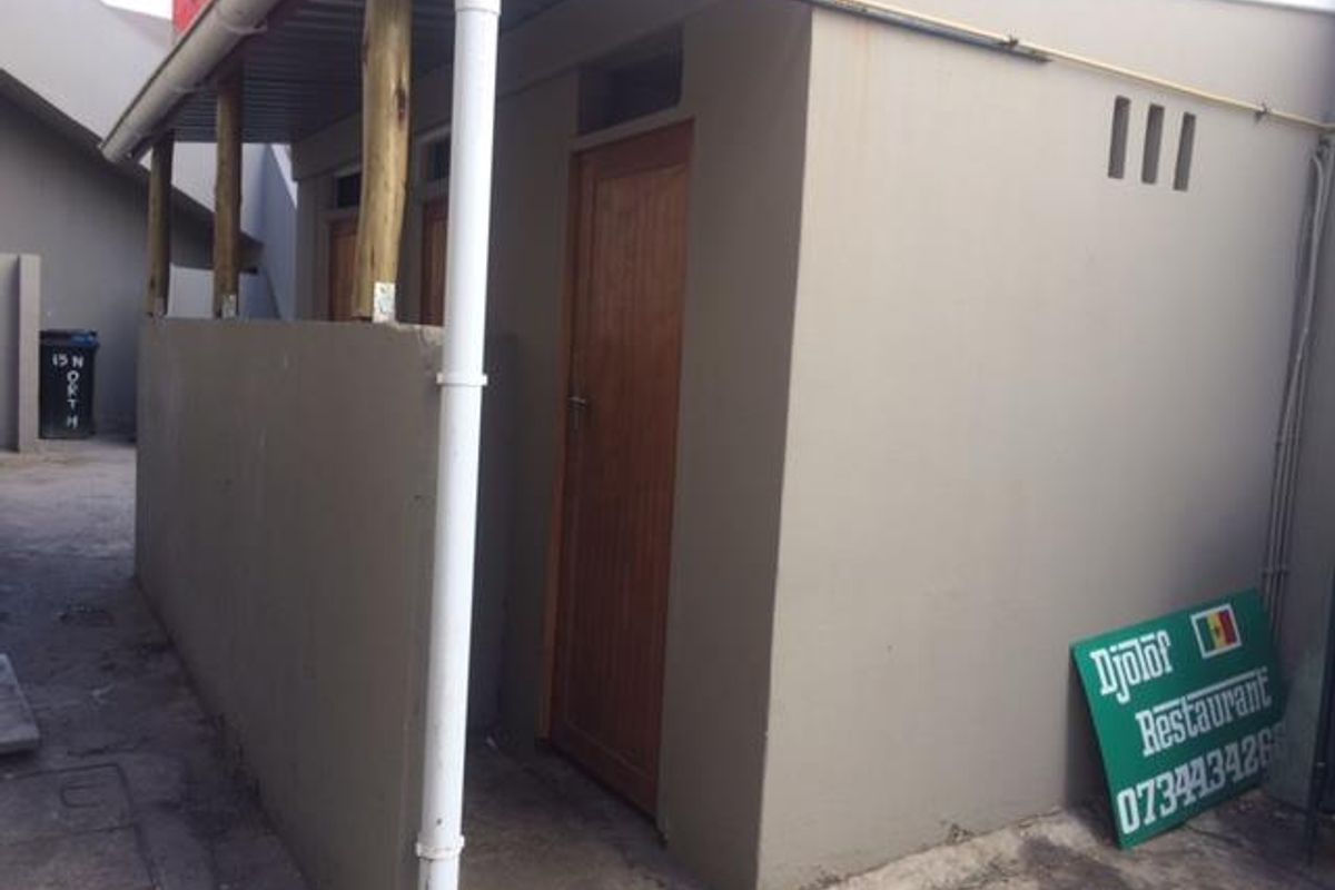 Rear exterior view of a commercial property featuring a covered walkway, wooden doors, and functional drainage infrastructure.