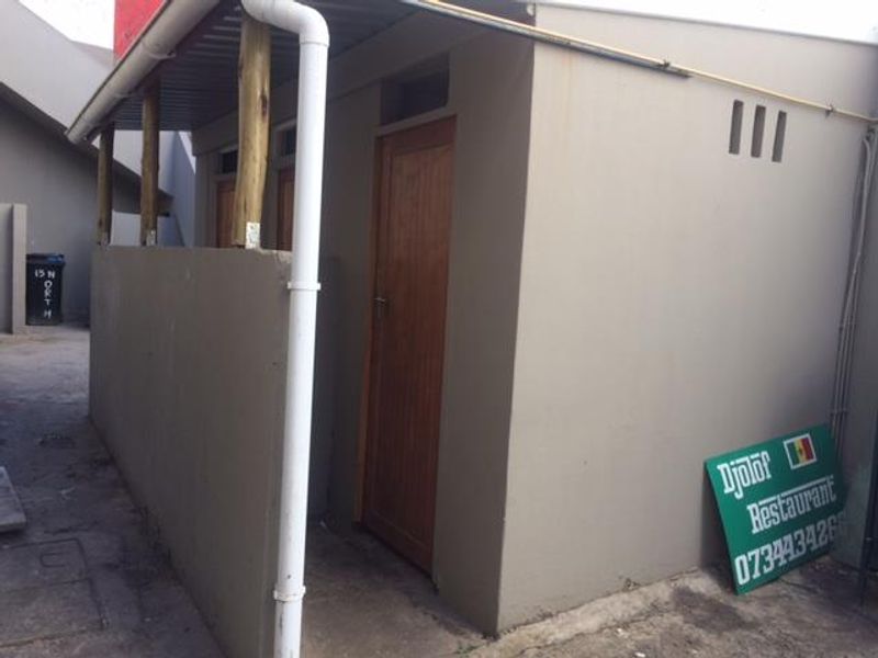 Rear exterior view of a commercial property featuring a covered walkway, wooden doors, and functional drainage infrastructure.