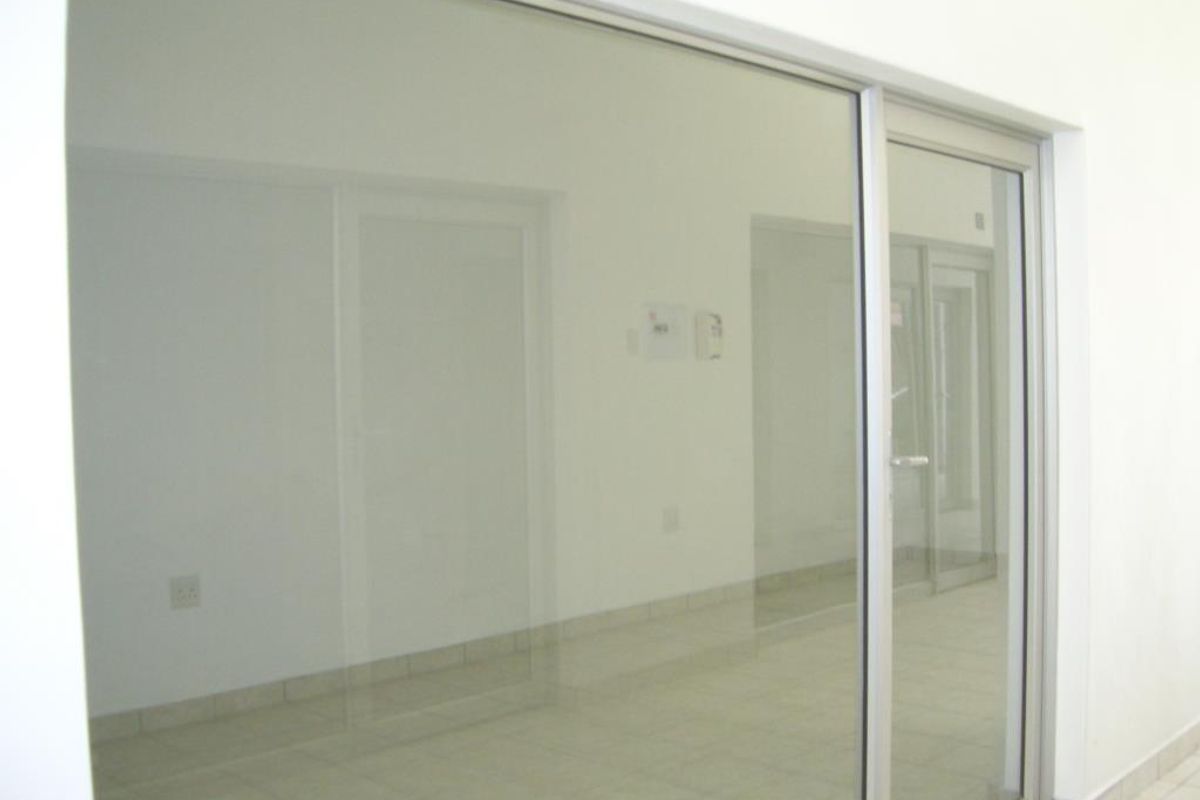 A bright, empty commercial office space featuring clean tiled flooring and modern aluminium-framed glass partitioning, suitable for a professional workspace.