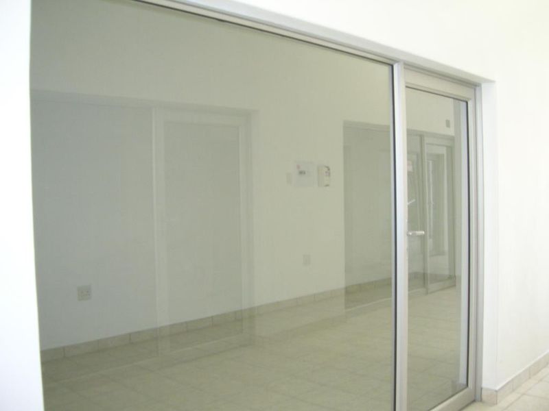 A bright, empty commercial office space featuring clean tiled flooring and modern aluminium-framed glass partitioning, suitable for a professional workspace.
