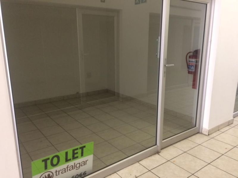 A vacant commercial entry space featuring ceramic tiled flooring and a large aluminium framed glass door, suitable for retail or office use.