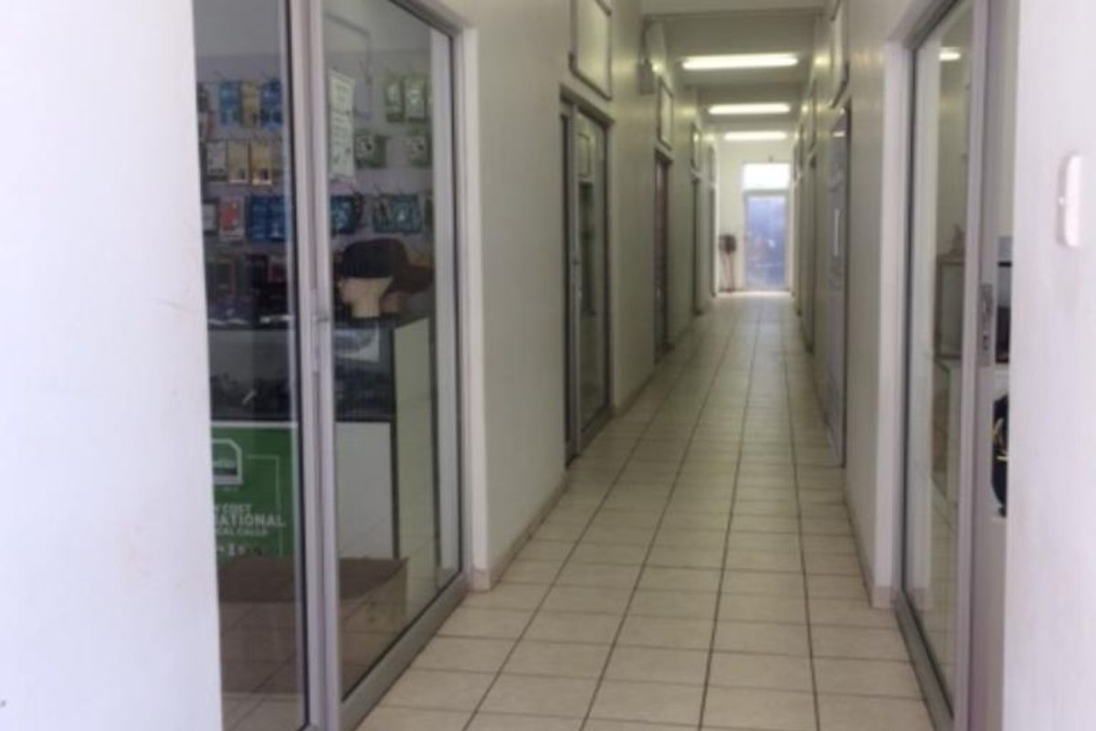 A commercial hallway featuring tiled flooring, fluorescent lighting, and multiple aluminium-framed glass entry doors leading into individual office or retail units.