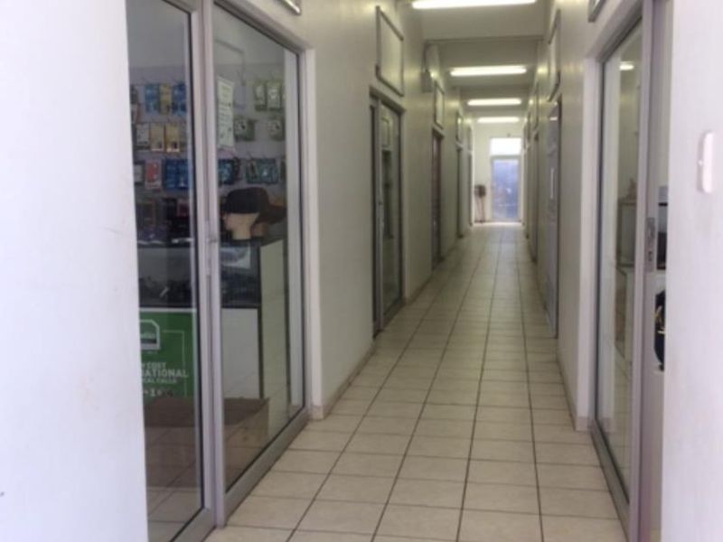 A commercial hallway featuring tiled flooring, fluorescent lighting, and multiple aluminium-framed glass entry doors leading into individual office or retail units.