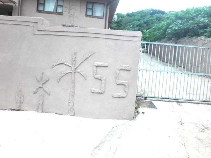Exterior view of the property entrance featuring a concrete boundary wall with decorative relief and a metal security gate.