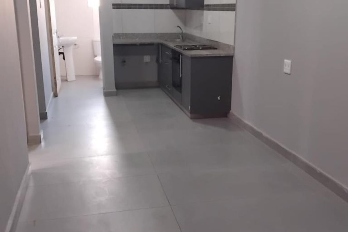 Open plan kitchen area featuring modern grey cabinetry, stone countertops, built-in oven and hob, with tiled flooring throughout.