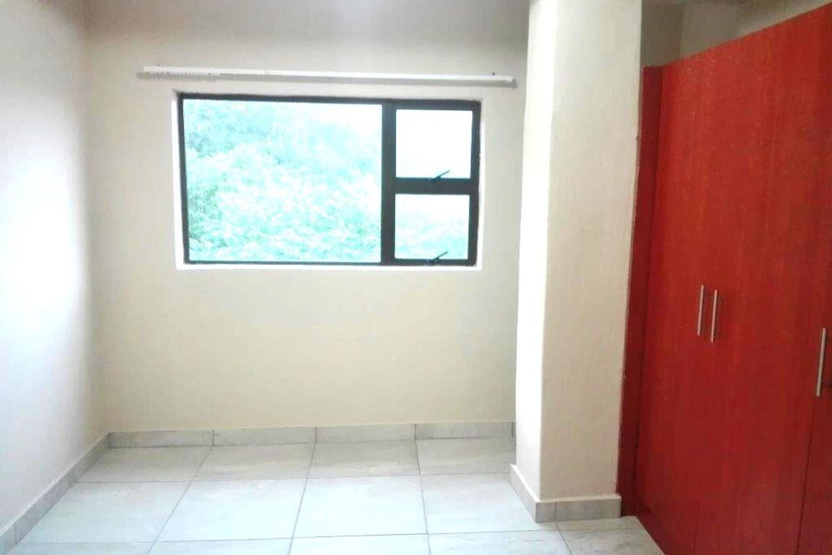 A bright bedroom featuring tiled flooring, a large window, and a built-in red wardrobe.