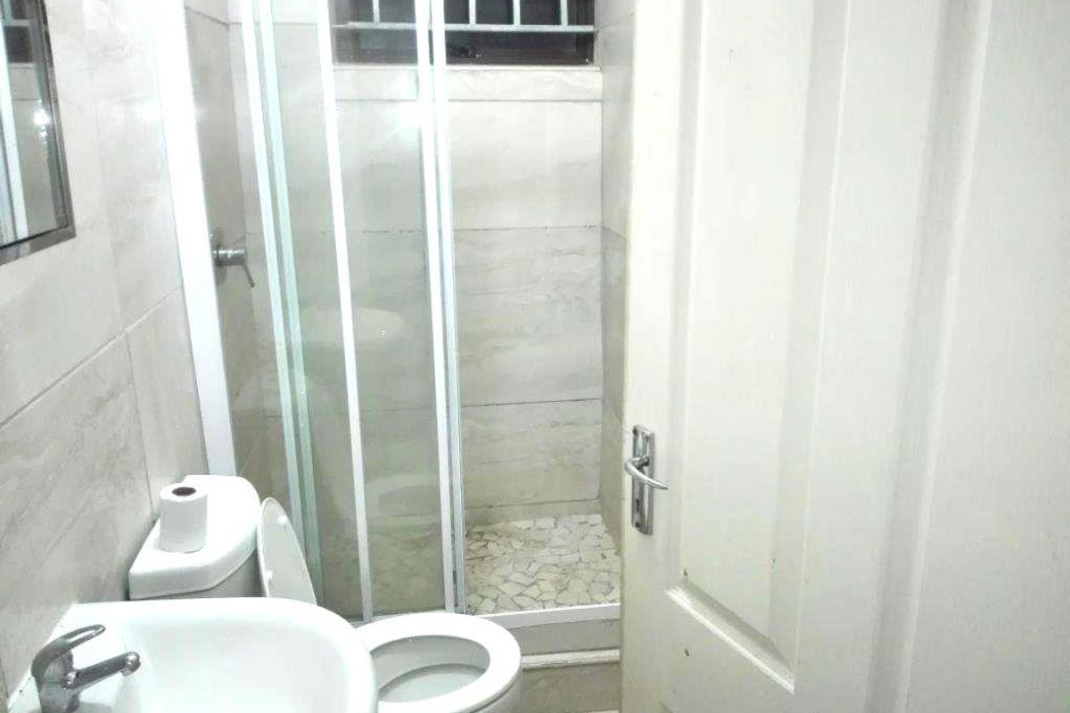 Compact bathroom featuring a tiled shower enclosure, pedestal basin, and toilet, finished with neutral wall tiles and a small high-level window.