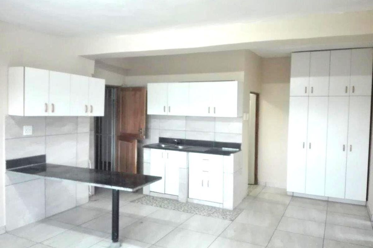 A functional kitchen featuring white cabinetry, dark stone countertops, a breakfast bar, and tiled flooring, offering a clean and practical layout.