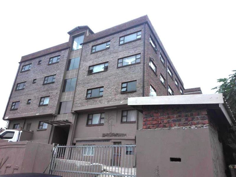 Exterior view of a multi-story apartment building featuring a brick facade, metal security gate, and ground-level entrance.