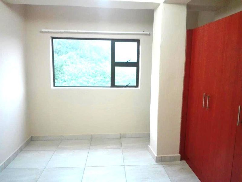 A bright bedroom featuring tiled flooring, a large window, and a built-in red wardrobe.